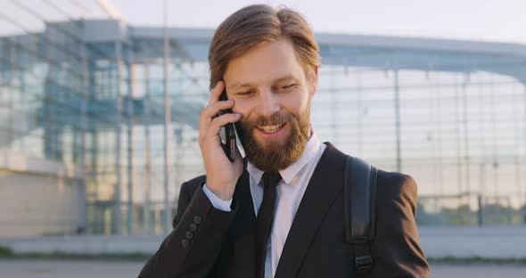 Man with Beard which Talking on Phone Near Big Modern City Glass Construction