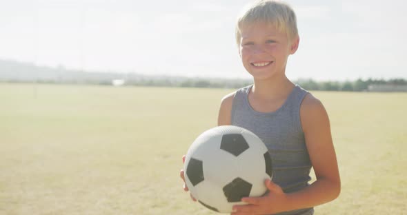 Video of happy caucasian boy holding ball on sports field