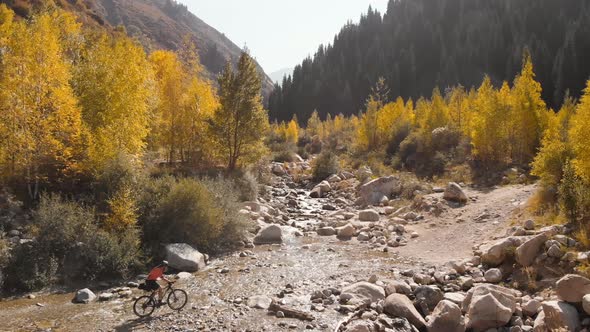 Man Is Crossing the River By Bicycle in the Mountains Shot By Drone