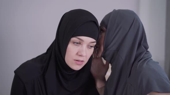 Portrait of Young Muslim Woman in Hijab Listening To Friend Whispering on Her Ear