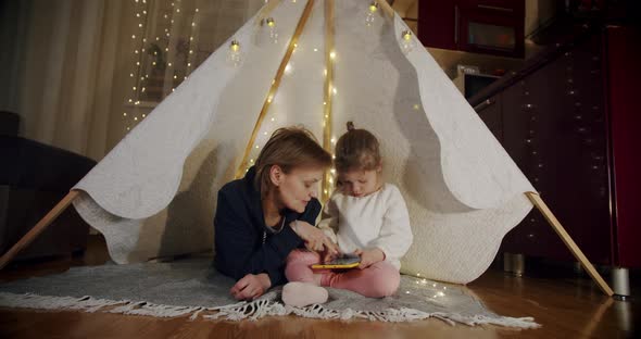 Happy Woman with Her Daughter at Smiling and Talking in Tent  Using Tablet