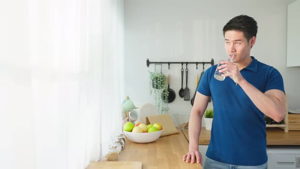 Portrait of Asian attractive male holding a glass of water in kitchen.