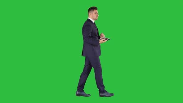 Elegant young businessman using his PC tablet while walking