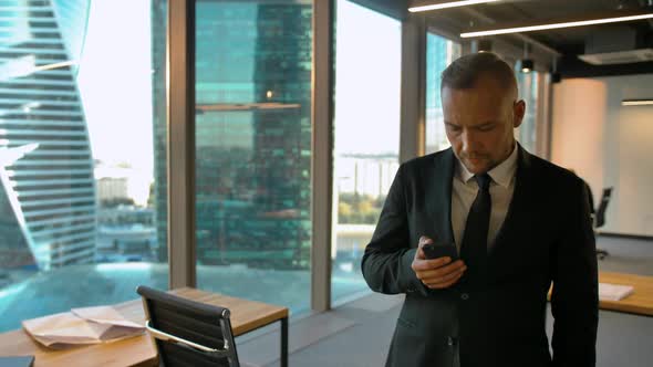 Attrtactive Entrepreneur in Formal Suit Standing Near Window and Writing Sms