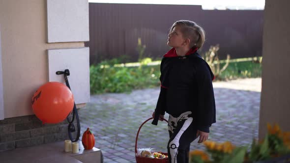 Cute Boy with Trick or Treat Basket Entering Decorated Porch on Front Yard Looking Around Leaving