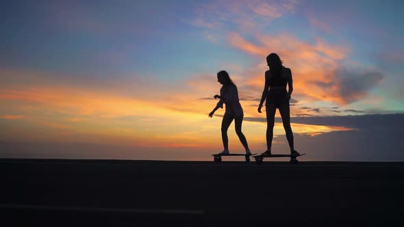 Silhouette of Girls on a Skateboard Ride on the Road Against the Rock and the Sky Beautiful at