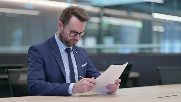 Middle Aged Businessman Reading Documents at Work