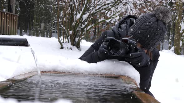 Woman taking photos of flowing water during winter season and snowfall