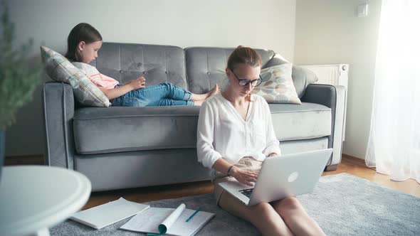 Young Woman Working From Home, While Her Daughter Lying on a Couch