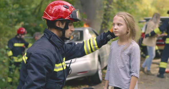 Firefighter Examining Girl Near Burning Car