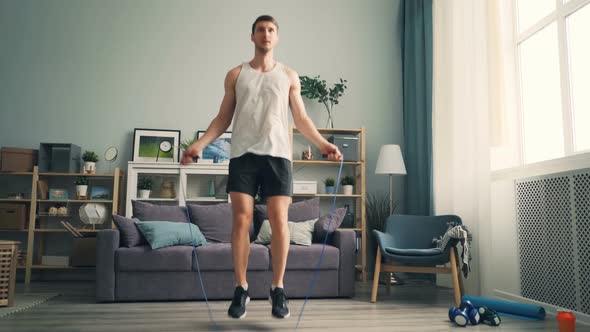 Young Man Jumping Rope Indoors at Home Wearing Sportswear and Sports Shoes