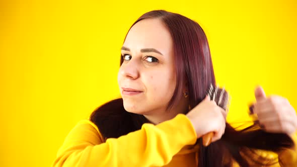 Portrait of Young Woman Combing Her Hair on Yellow Background