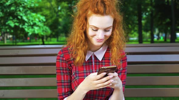 Positive Redhead Girl Texting Message on Phone in Green Park