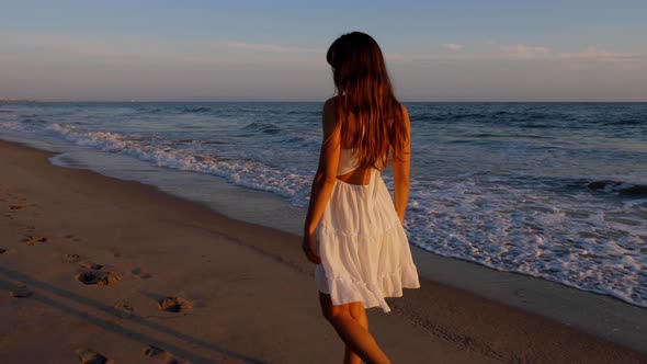 Beautiful woman in a white dress at the beach at sunset