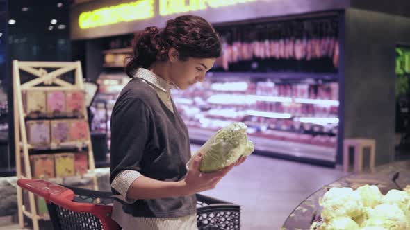 Young Beautiful Brunette Girl in Her 20's Picking Out Napa Cabbage and Cauliflower and Putting Them