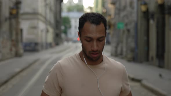 Male Runner is Running in the Old Town Street and Listens to Music