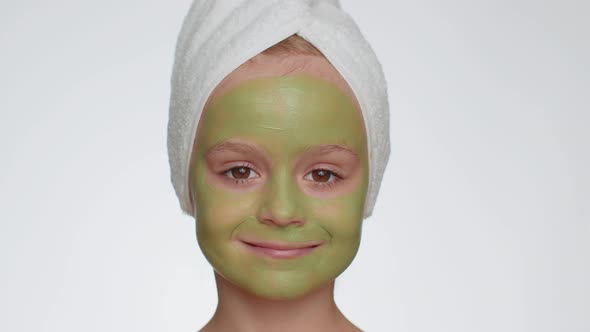 Beautiful Smiling Child Girl Kid in Towel on Head Applying Cleansing Moisturizing Green Mask on Face