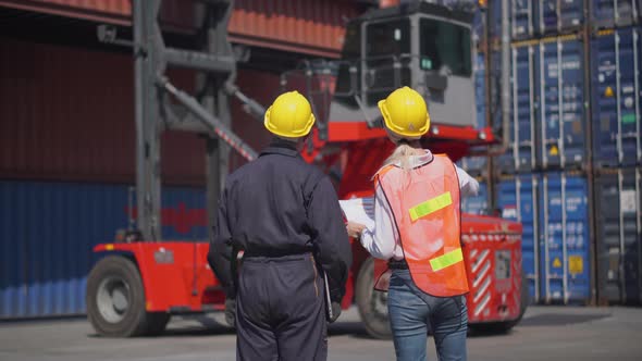 Engineer and foreman team in hardhat and safety vest control loading containers box from cargo