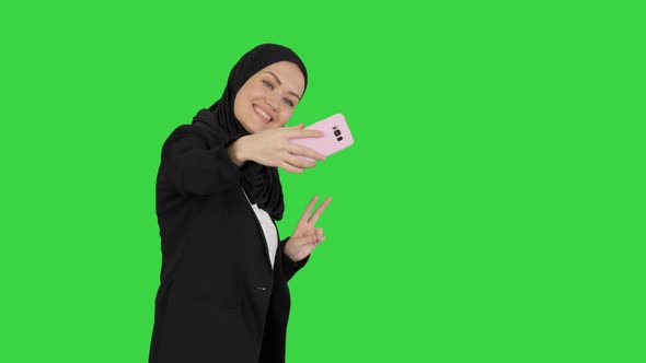 Smiling Arab Woman in Hijab Taking Selfies on Her Mobile Phone As She Walks on a Green Screen