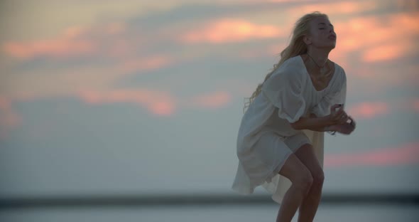 Pretty Woman in White Dress is Dancing on a Pier During Sunset