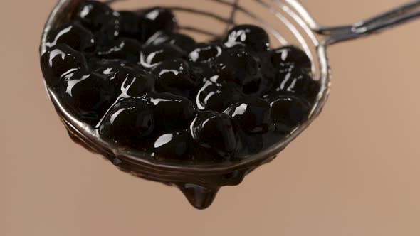 Close up on Steel Spoon with Sticky Black Tapioca Pearls Falling, Soft Background