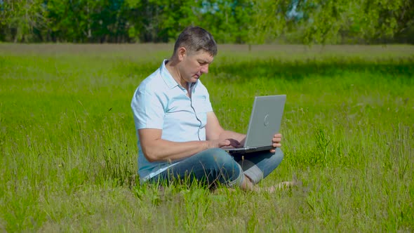 Businessman Works Behind a Laptop Sitting on the Grass