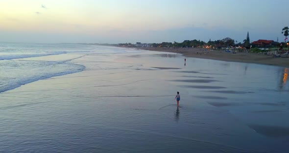 Aerial drone view of a young woman walking on the beach at sunset.