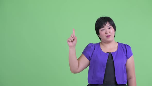 Happy Young Overweight Asian Woman Pointing Up and Talking