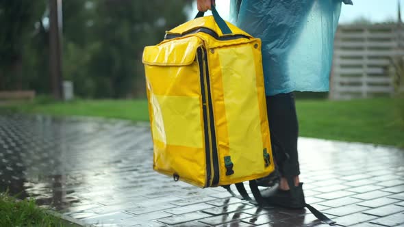 Tracking Shot of Yellow Delivery Bag in Hand of Unrecognizable Courier in Rain Coat Walking in Urban