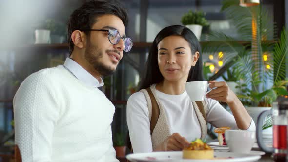 Asian Woman and Arab Man Drinking Tea and Talking on Date in Cafe