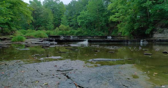 Drone footage over a riverbed with five waterfalls in the background.