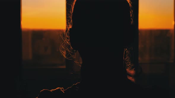 Silhouette of Young Woman Goes to the Window at Sunset Rear View Slow Motion