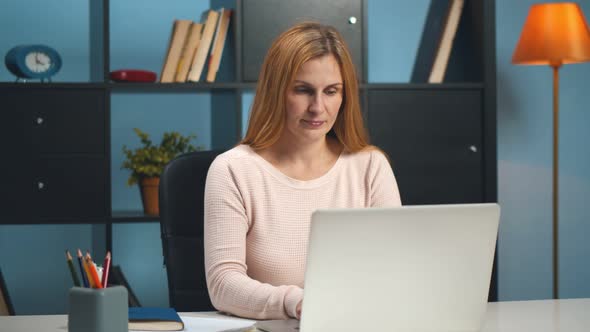 Mature Businesswoman Sitting at Workplace in Office and Working on Laptop