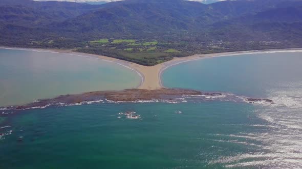 Aerial shot pulling away from the whale tail shaped rocky point of Punta Uvita with blue waters and