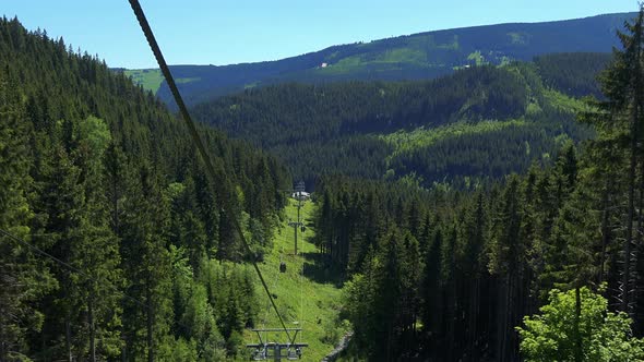 Forest with Trees Surrounding Aerial Tramway on the Mountain in Sunny Summer Day - Aerial Shot