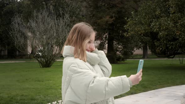 Young Girl Doing Hairstyle and Looking at Smartphone in Park