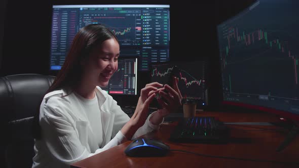 Female Stock Market Broker Using Mobile Phone With Analysing Graphs On Multiple Computer Screens