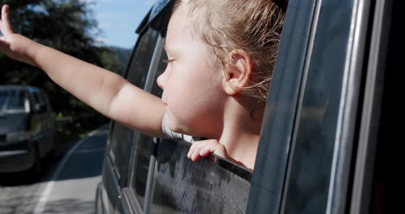 Happy Cute Little Girl with a Smile Stuck Out of the Car Window Into the Wind. Slow Motion V3