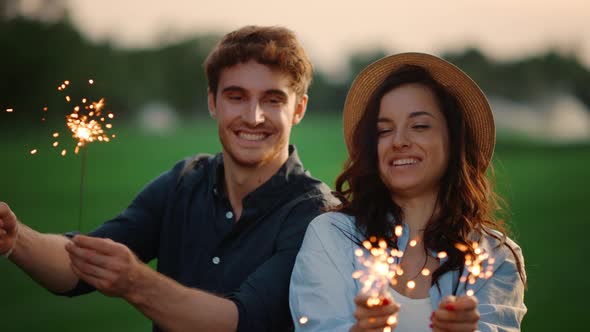 Happy Couple Playing with Bengal Lights on Meadow. Couple Enjoy Party Outdoors