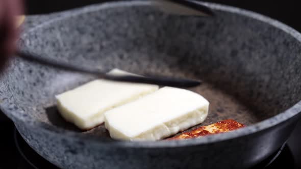 Fry halloumi cheese in a gray frying pan.