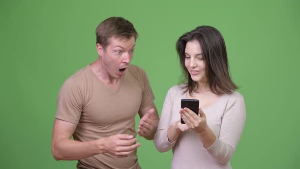 Young Woman Using Phone with Young Man Looking Shocked