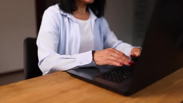 Mature woman typing something on laptop, working on computer at home