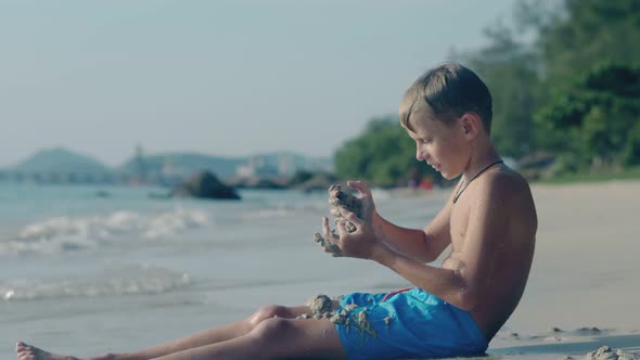 Joyful Boy Sits and Throws Wet Sand on Pictorial Ocean Beach