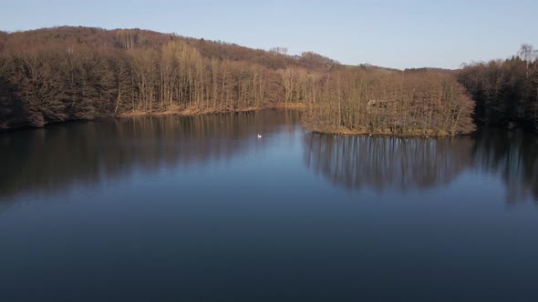 Big blue lake and leafless brown trees on its shores during a vibrant sunset in winter. Low flyover