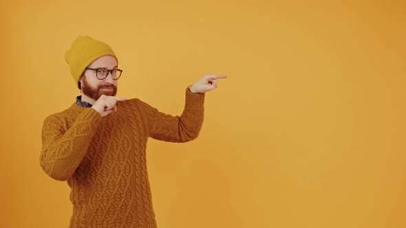 Young European Bearded Hipster Guy Pointing with Both of His Index Fingers at Copy Space Next to Him