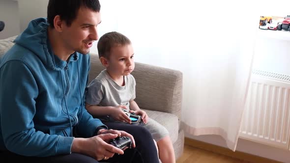 Happy Father and Son Sit in the Living Room on the Sofa and Play or Watch TV