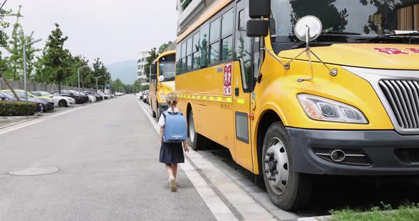 Schoolgirl Wearing School Uniform and Backpack and Standing Near Yellow Bus