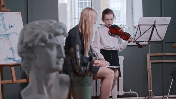 Young Woman Teacher Giving a Violin Lesson to a Little Smiling Girl in the Class Greek Man Bust and