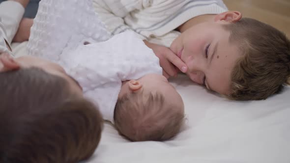 Boy Gesturing Hush Finger on Lips in Slow Motion Admiring Baby Girl Lying on White Bed at Home