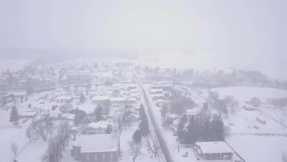 High aerial drone shot flying over a small village during a blizzard